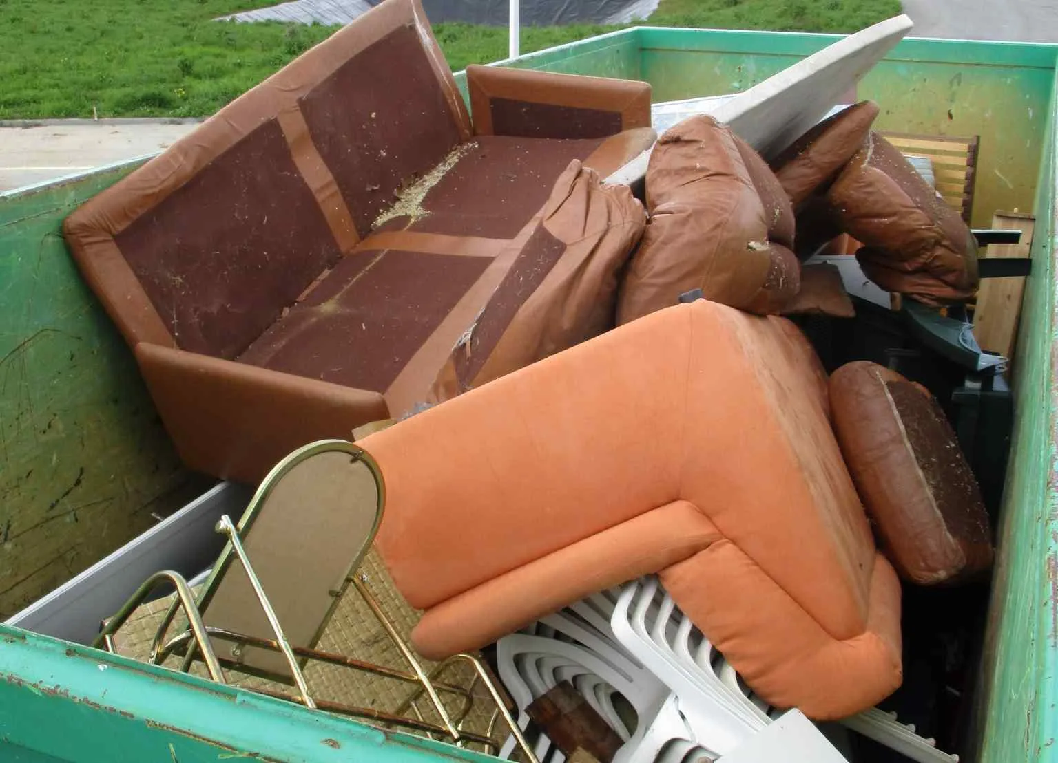 Une benne remplie de meubles mis au rebut, y compris des canapés, des coussins, des chaises et divers articles ménagers.
