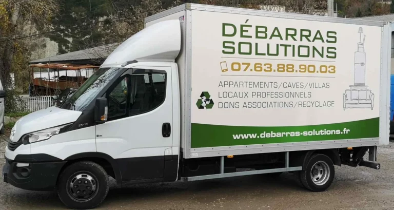 Un camion-caisse blanc portant la marque "Débarras Solutions", un numéro de contact et une liste de services pour le nettoyage des espaces, les dons et le recyclage.