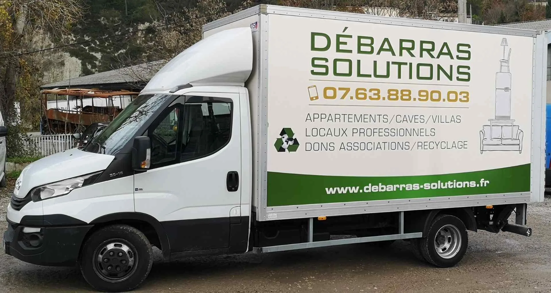 Un camion-caisse blanc portant la marque "Débarras Solutions", un numéro de contact et une liste de services pour le nettoyage des espaces, les dons et le recyclage.